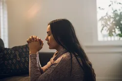A woman kneels in prayer asking for strength and hope through the power of Jesus Christ