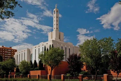 The Madrid Spain Temple exterior in the daytime, surrounded with trees, with a cloudy sky beyond.