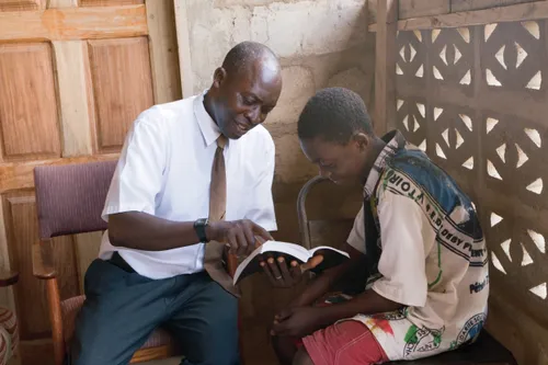 A father sits outside with his son and reads the scriptures with him.