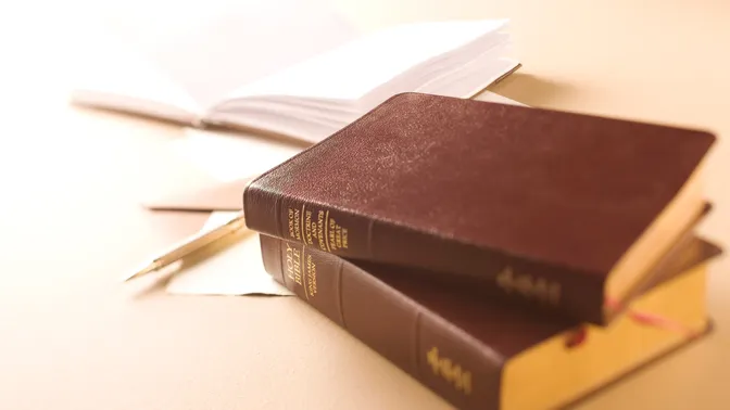 A bible and triple combination on a table with papers.