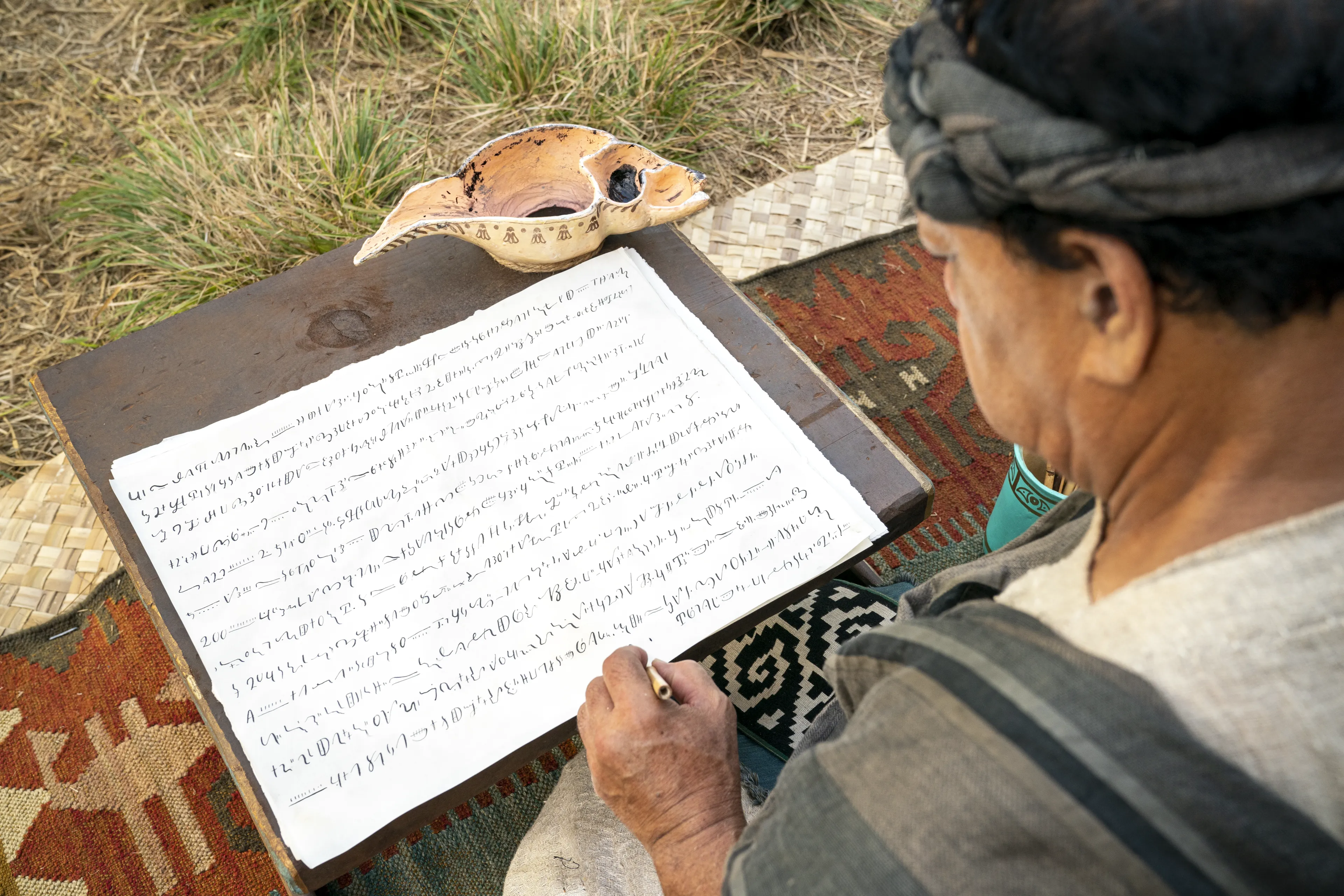 Scribes sit, taking notes on parchment of what King Benjamin is teaching in the Land of Zarahemla.