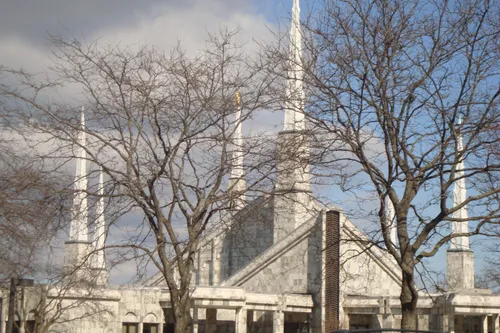 The spires on the Chicago Illinois Temple seen through the branches of bare trees in the winter, with a large gray cloud in the background.