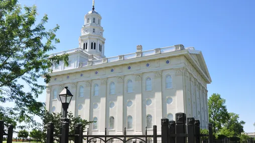 Side view of the Nauvoo Illinois Temple on a sunny day. The building is Greek Revival architectural style constructed from white stone. 