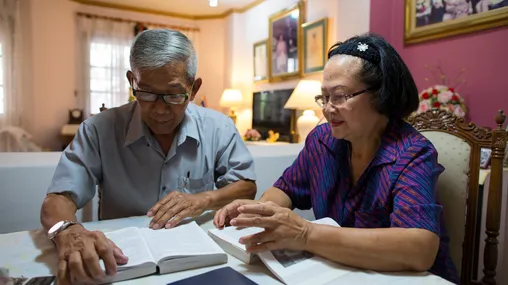 a couple in Thailand sitting together studying. A man also joins them for a time.