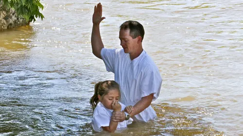a father baptizing his daughter in a river