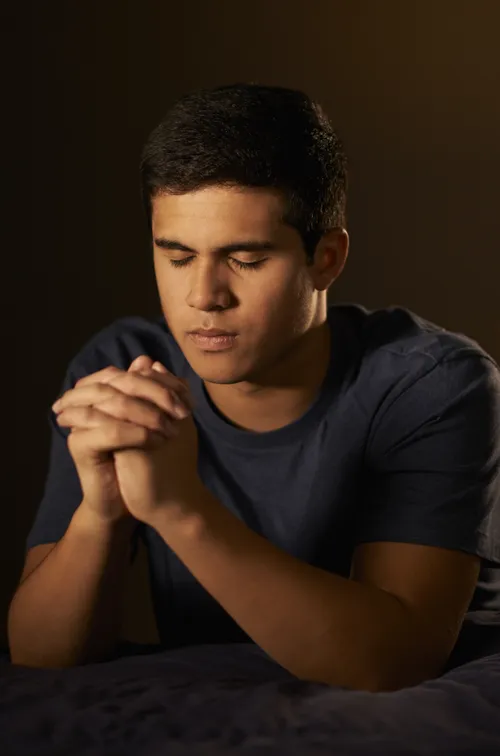 A young man kneeling by his bed in prayer.