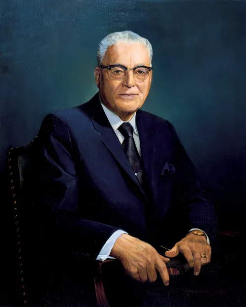 A painted portrait by David Ahrnsbrak of President Harold B. Lee in a dark blue suit, sitting in an armchair and holding scriptures.