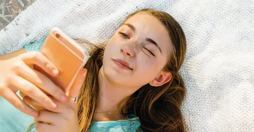 Confused Caucasian girl laying on blanket texting on cell phone - stock photo