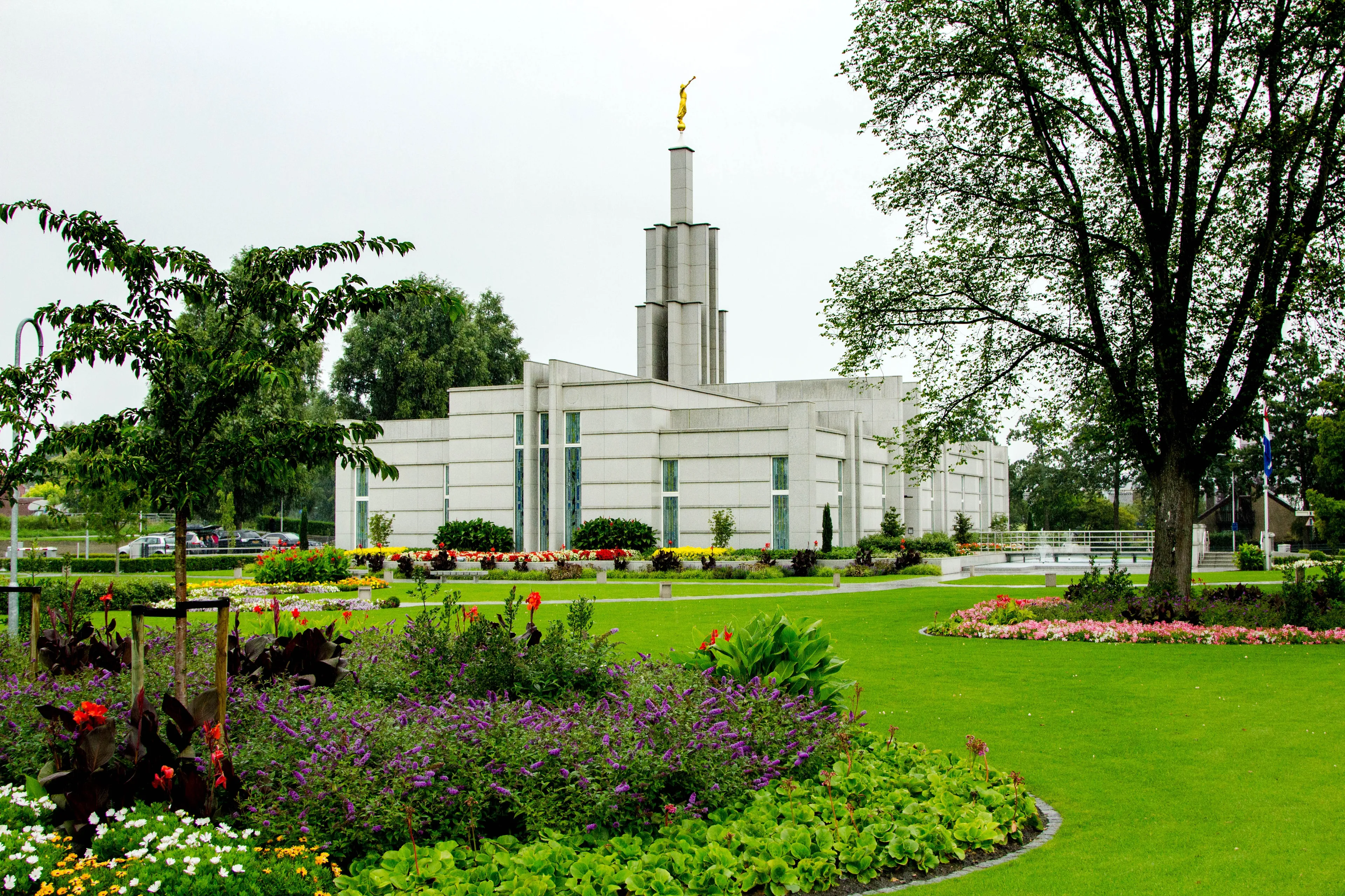 The Hague Netherlands Temple on a cloudy and rainy mid-summer day. Trees, shrubs, flowers, and green grass help beautify the Temple grounds.