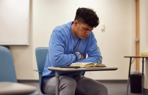 a young man sitting at a desk and studying his scriptures