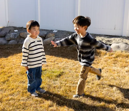 Two children outside, one is standing still, the other is running with his arms out