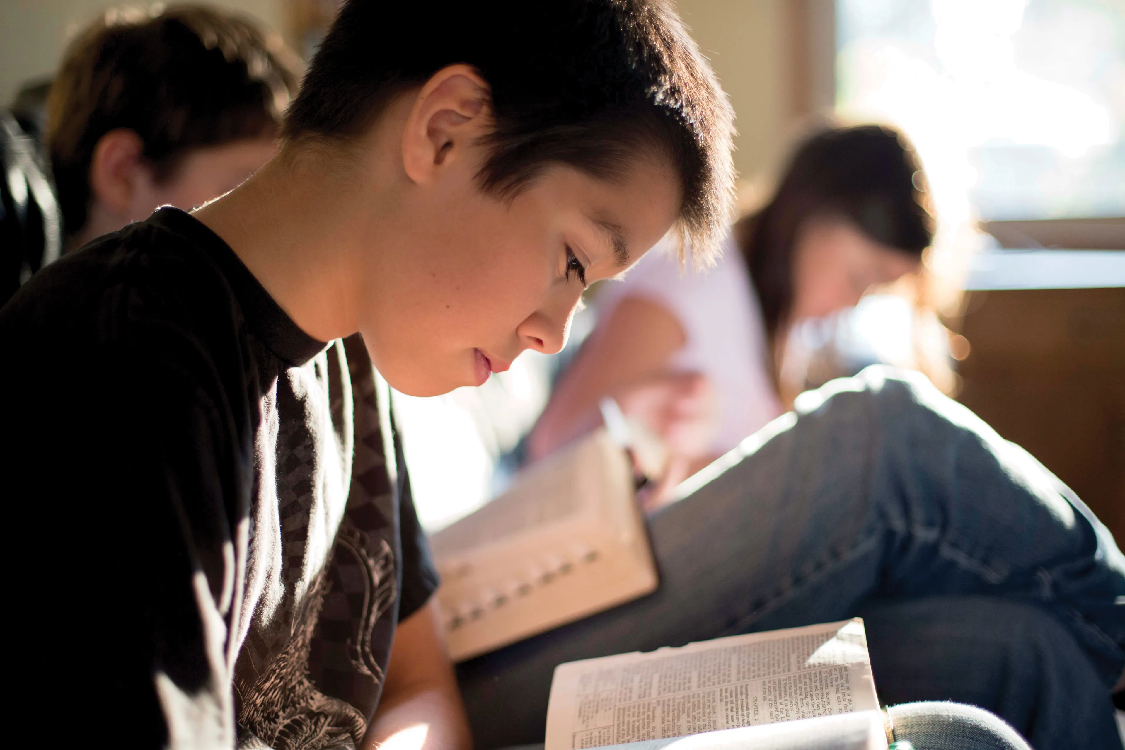 A young boy reads his scriptures with his family.