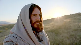 Jesus is standing on a hill. You can see the sun in the background