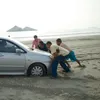 people pushing a car stuck in the sand