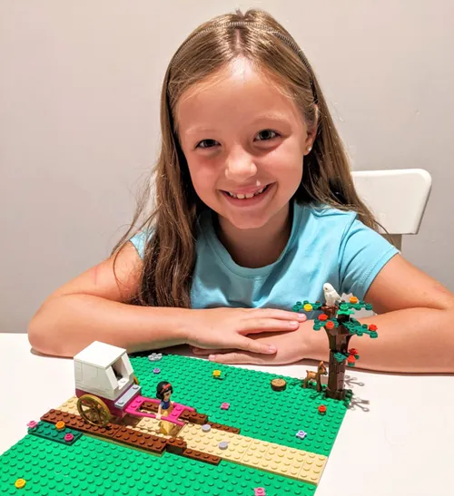 A young boy sits with a stack of Legos. It appears to be a temple he has created.