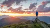 man standing on mountain top and looking at sunset