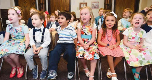 Primary-age children sing while seated on chairs.