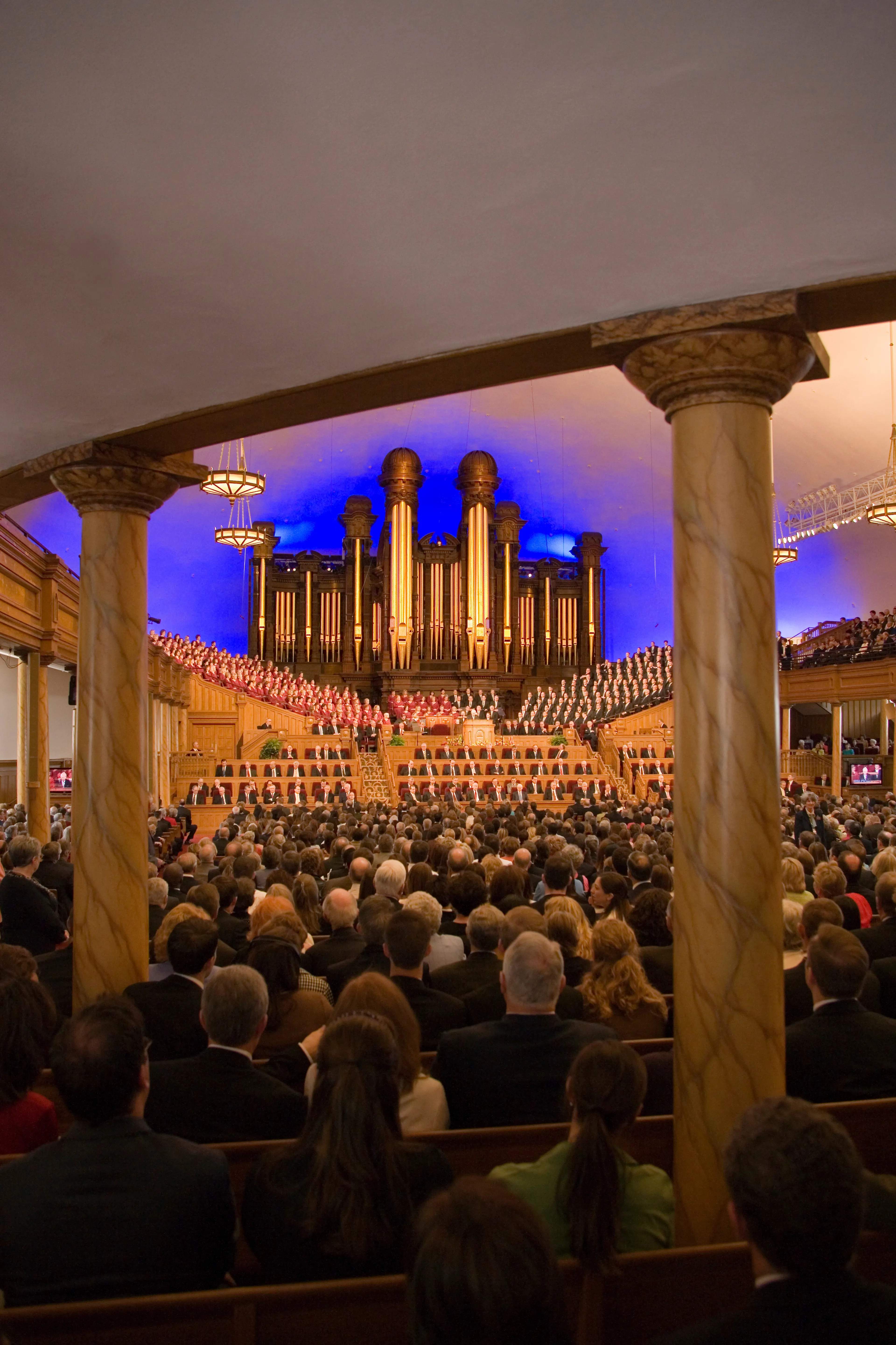 A view from the back of the Salt Lake Tabernacle interior, with people sitting on benches.