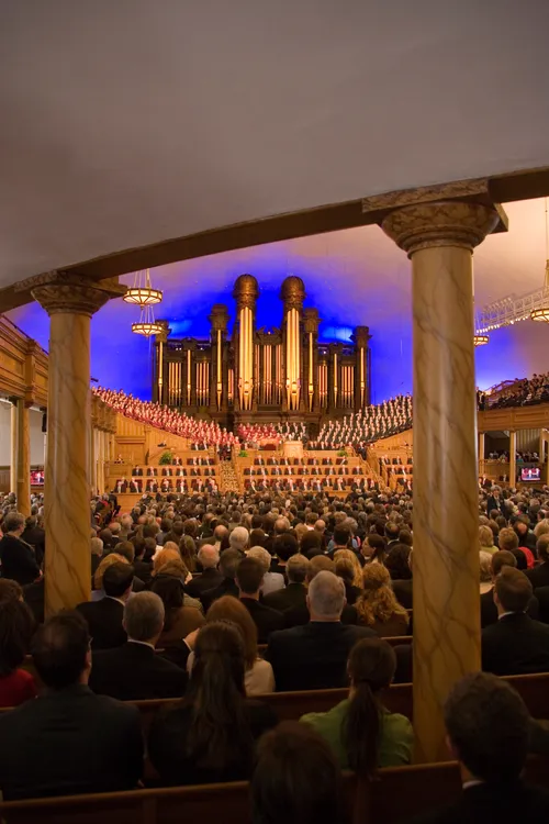 A view from the back of the Salt Lake Tabernacle, showing two pillars and many rows of benches filled with people.