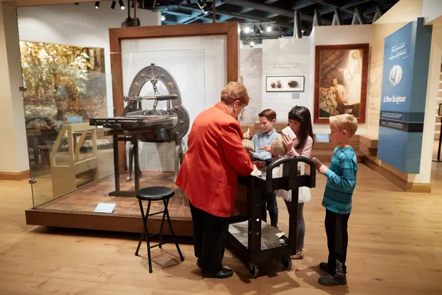 Children in the Church History Musuem. A group of children interact with the exhibits. A docent is nearby talking with them.