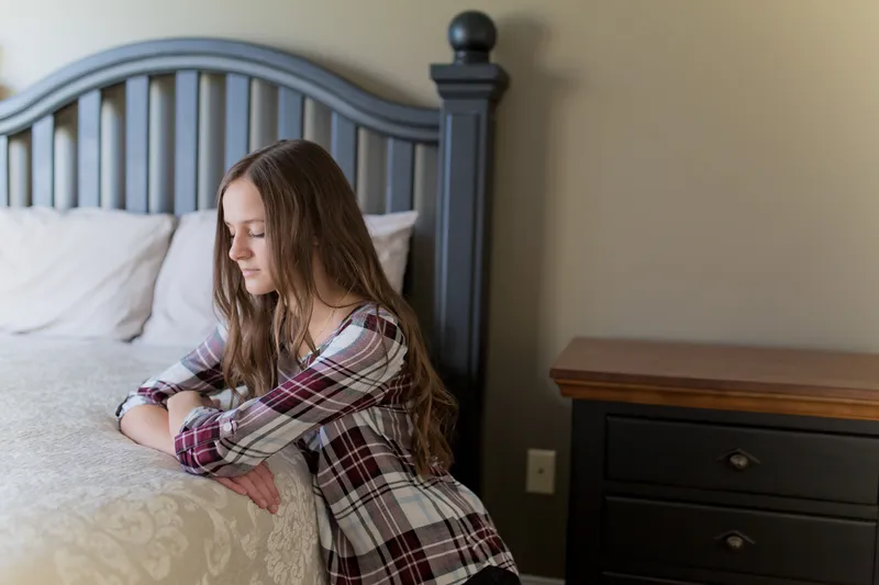 A young woman kneels at her bedside praying for guidance from God