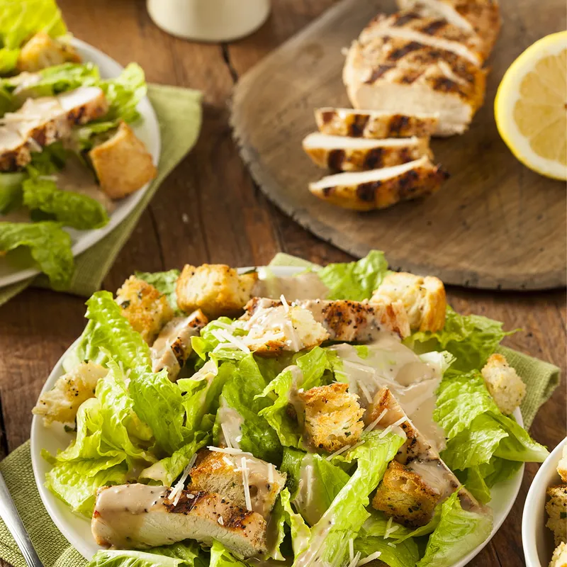A salad with pieces of chicken and lemon wedge on a kitchen table