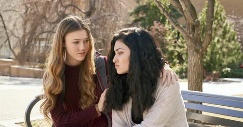 two young women sit together on a bench