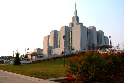 The Calgary Alberta Temple in the daylight, with an orange and green bush in the foreground.