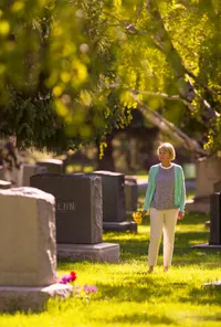Frau mit Blumen bei Grabsteinen auf einem Friedhof