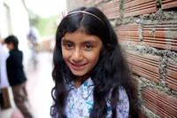 A portrait of a young girl with long brown hair and a floral patterned shirt, smiling.