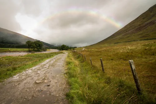 A dirt road is flooded with water after a heavy rain. There is a slight rainbow.