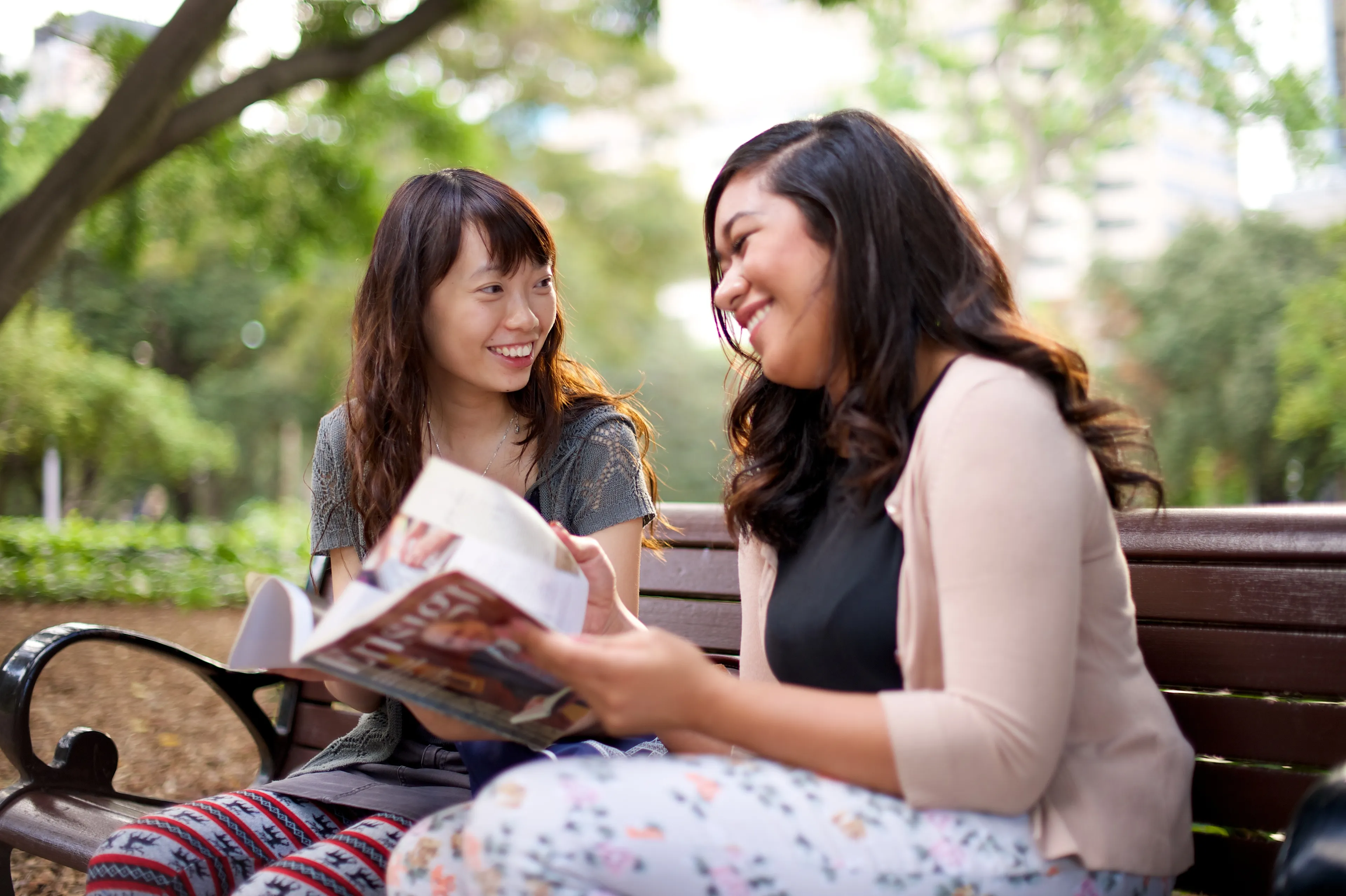 Two young women sit on a bench and read from the Ensign.