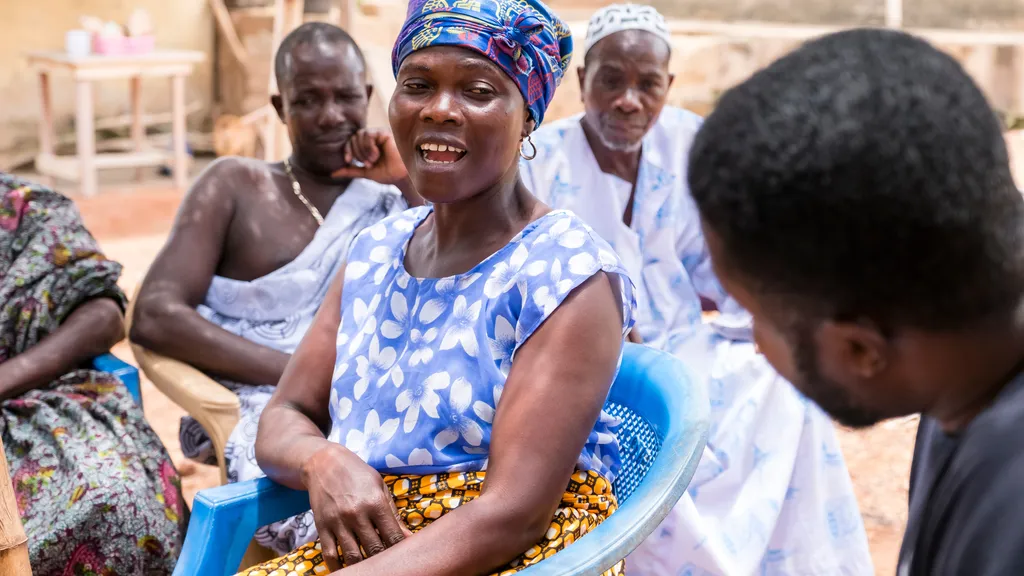 People sitting under a twig bowery listening to a team of people helping collect oral histories.