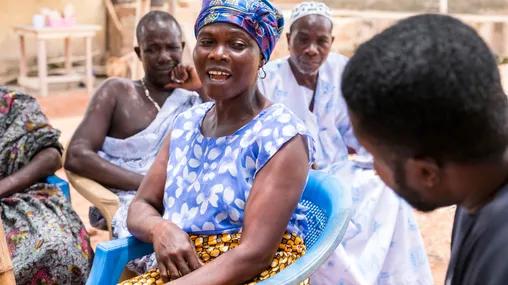 People sitting under a twig bowery listening to a team of people helping collect oral histories.