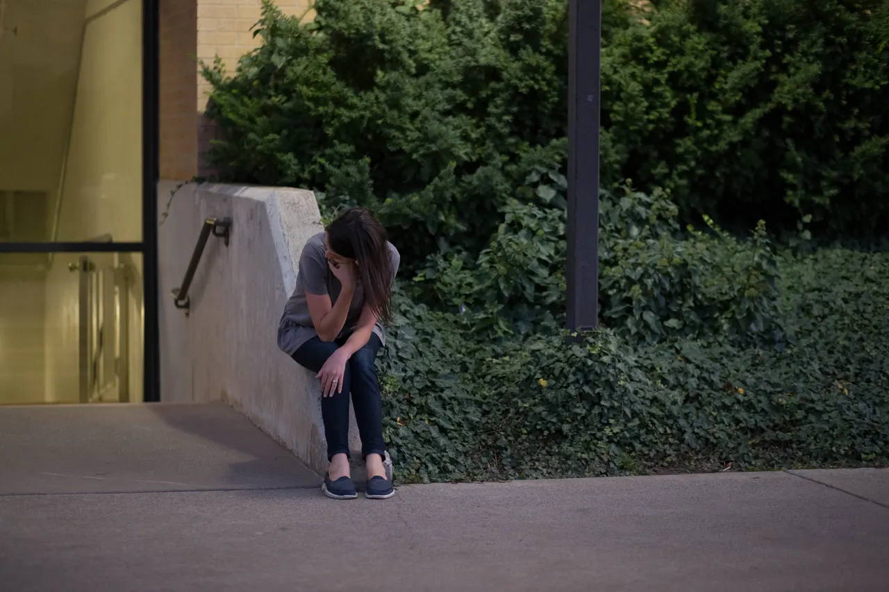 A woman sits on a concrete block outside of a building