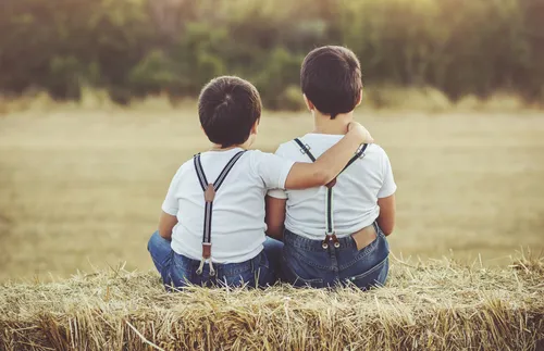 two boys sitting on a bail of hay together