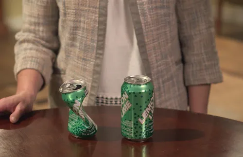 Woman with 1 can of soda that is crushed and one that is not.