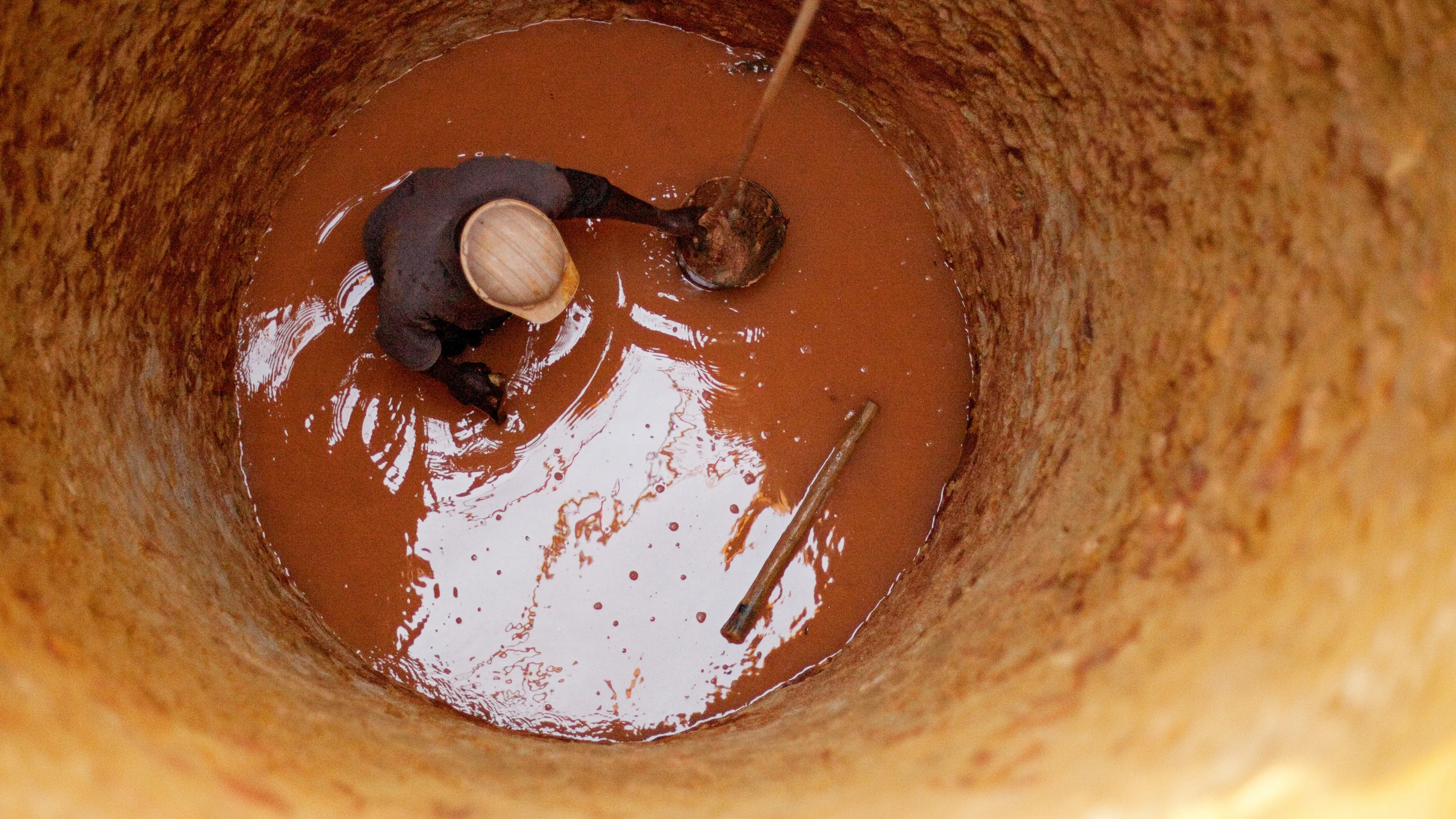 A man working knee-deep in water inside of a well.