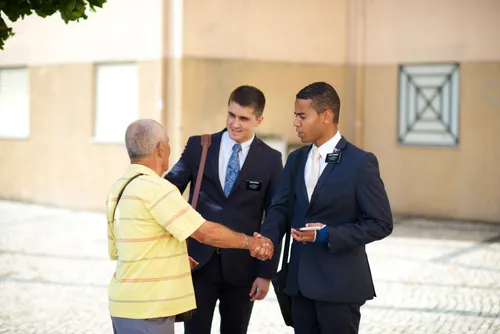 An elderly man in a yellow shirt shaking hands with two elder missionaries while standing in a street in Portugal.