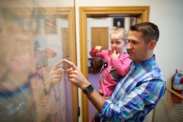 A father is with his children. They are inside the Beehive House (home of Brigham Young) in Salt Lake City, Utah. They all interact with the exhibits in the museum.