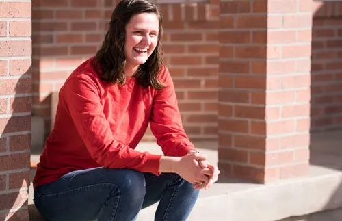 Young adult woman sitting outside of a brick building.