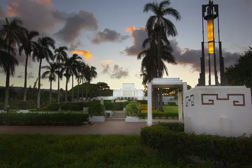 The grounds of the Laie Hawaii Temple at sunset, with rows of palm trees and manicured bushes.