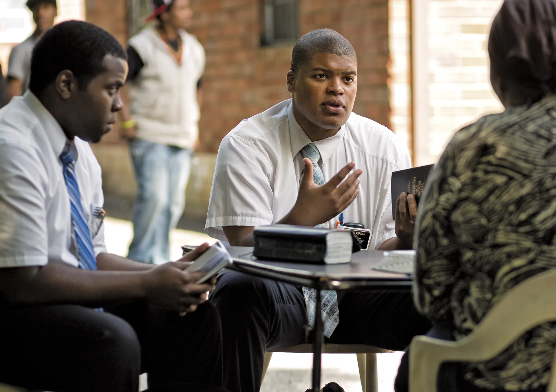 A woman sitting across from two elder missionaries who are teaching her the gospel.