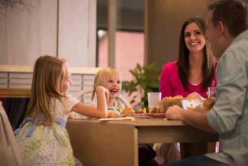 Parents and two young girls sitting at a table eating dinner.
