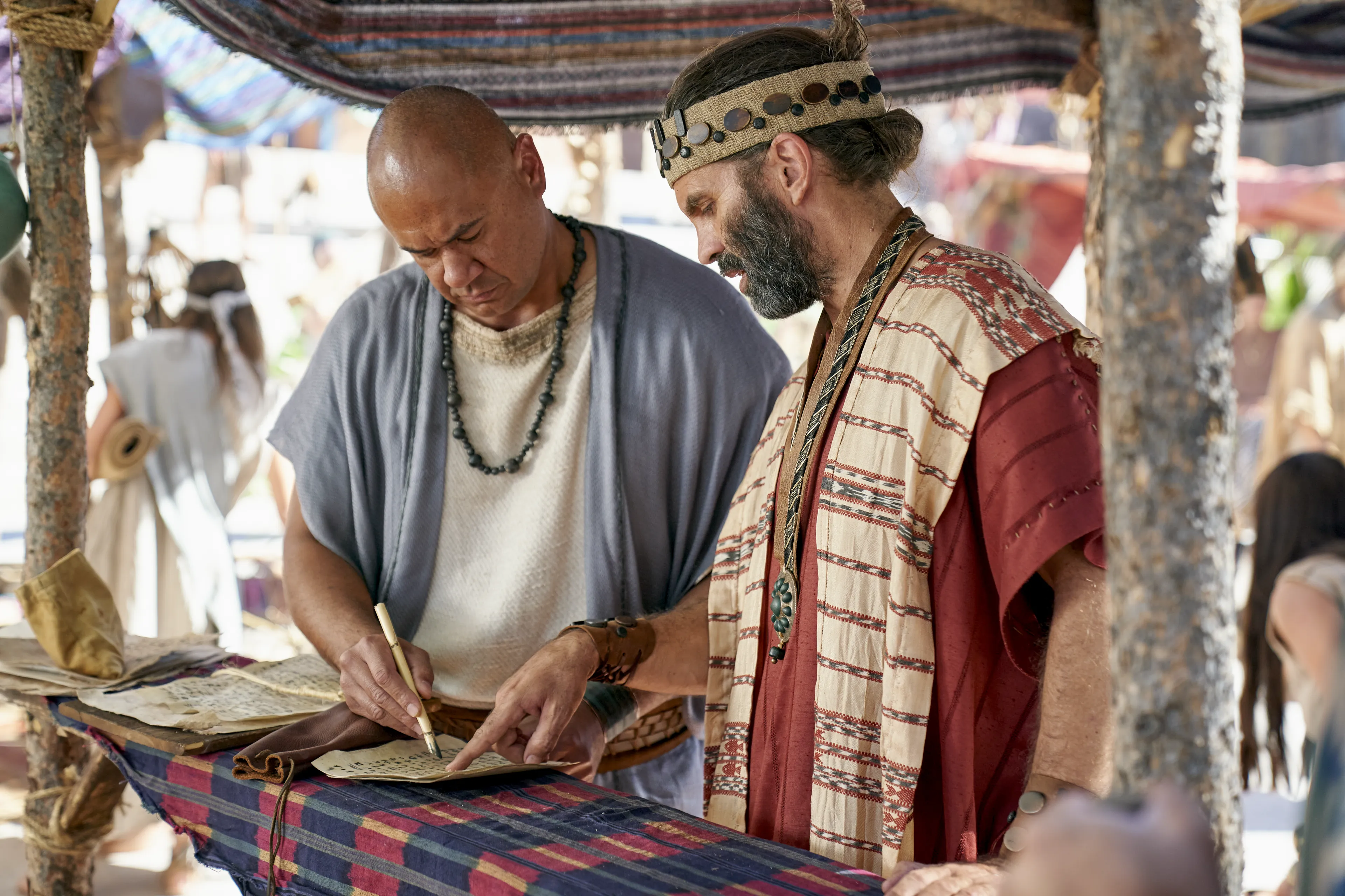 Zeezrom speaks with a lawyer as he writes on parchment in the city of Ammonihah.