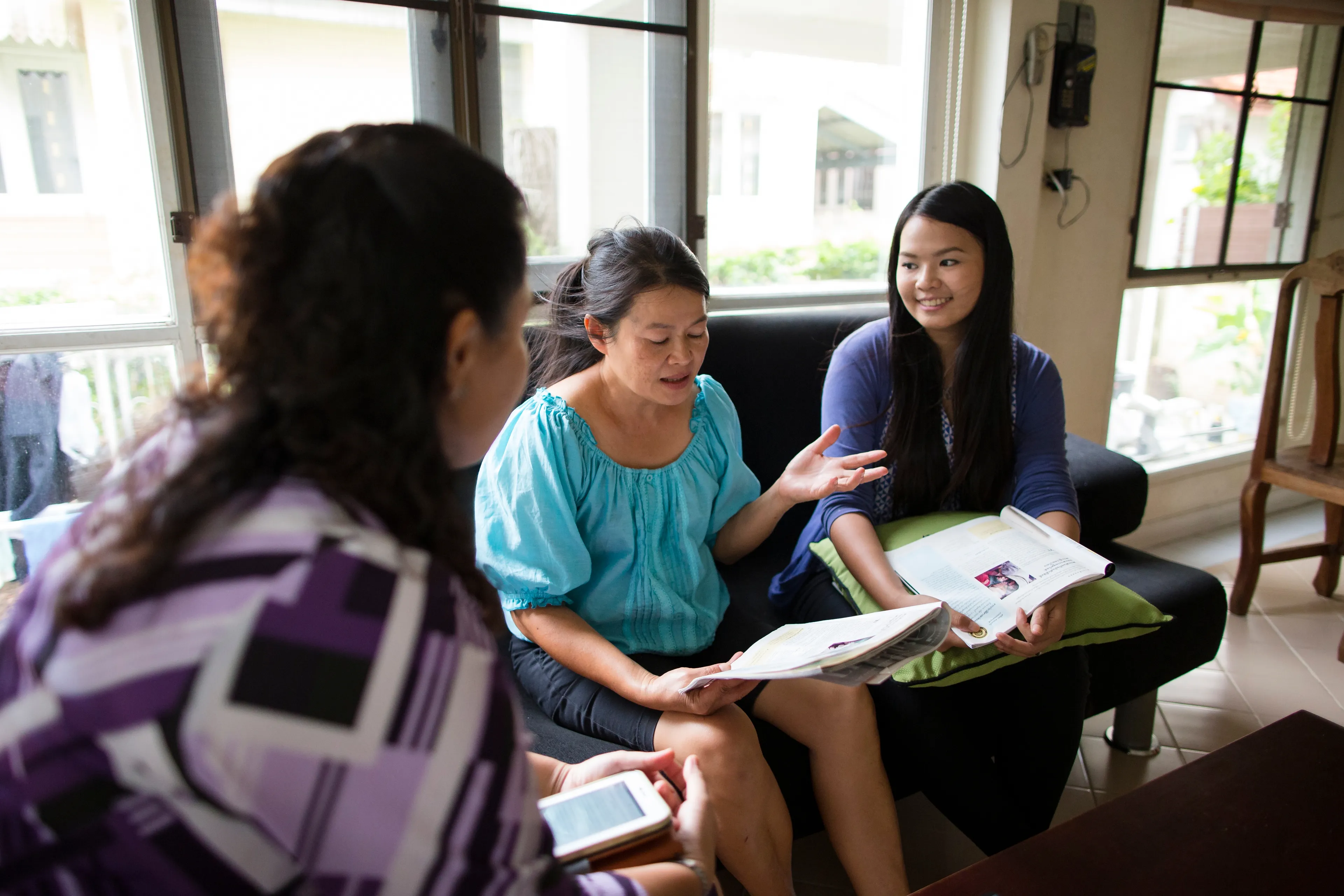Three women from Thailand sitting and studying from magazines.