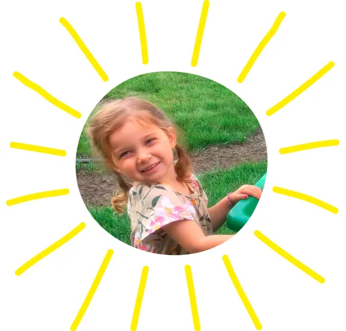 A young girl holds on to a wheel barrel made into a handcart.  She is dressed in a pioneer dress.