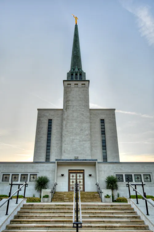 The front steps of the London England Temple leading up toward the temple doors, with the temple’s spire and the angel Moroni statue overhead.