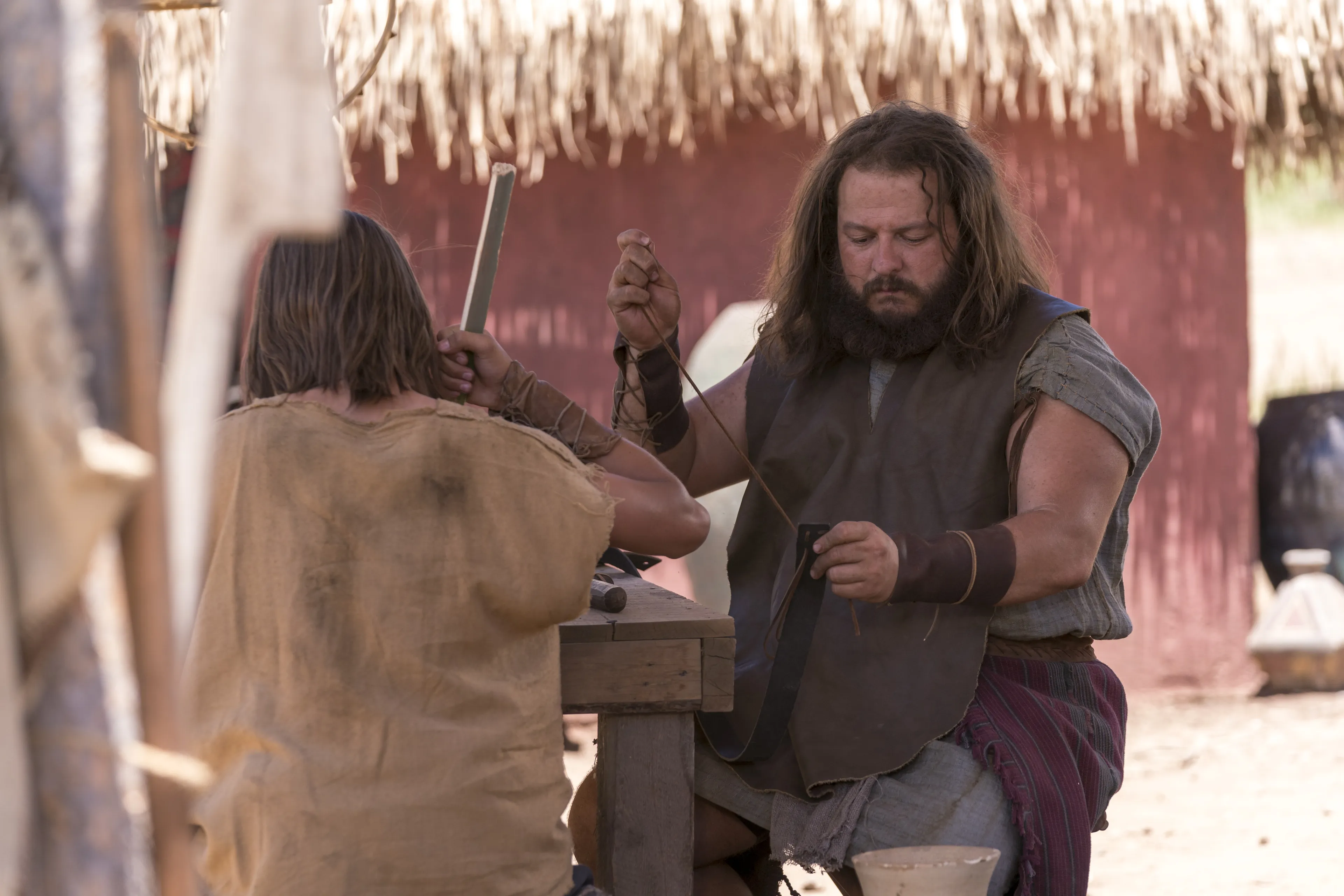 Zoram sits at a table working with leather.