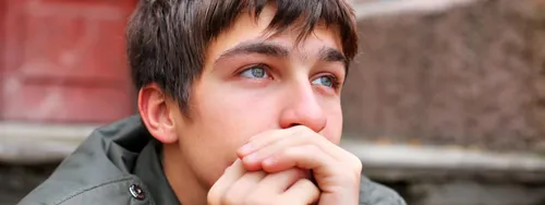 A young adult man sits on some stairs and places his head in his hands. He appears to be thinking about something.